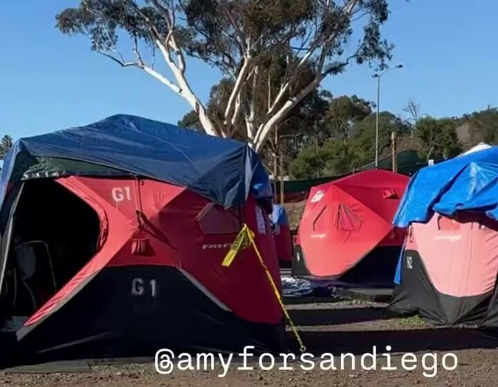 Carpas rojas desplegables cubiertas con lonas en un terreno de tierra en un sitio Safe Sleeping administrado por la ciudad